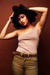 pretty young african american woman with curly hair posing cheerful gesturing on brown background, lifestyle people concept