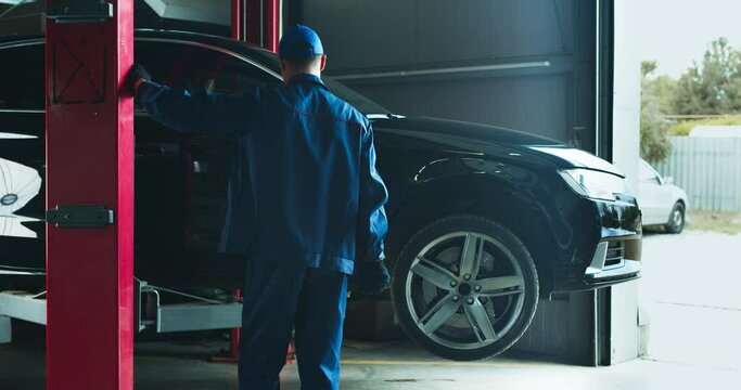 Car service worker lifting vehicle on hoist before maintenance at service workshop