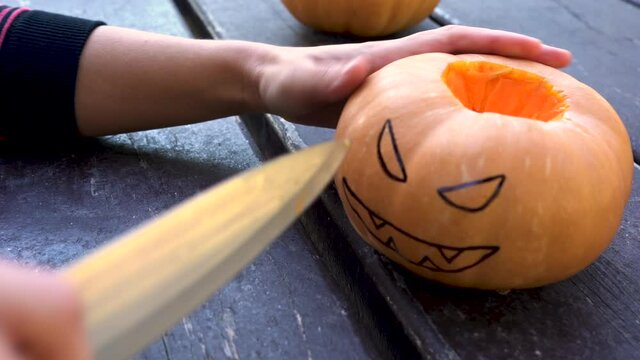 Hand uncovers pumpkin and begins to cut painted face with marker pen