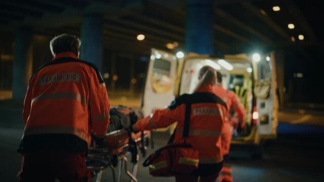 Team of EMS Paramedics React Quick to Provide Medical Help to Injured Patient and Get Him in Ambulance on a Stretcher. Emergency Care Assistants Arrived on the Scene of a Traffic Accident on a Street.