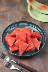 Buah Semangka or watermelon fruits, served on ceramic grey plate with fork beside, brown grainy background. Selective focus, close up. 