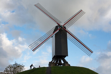 Historic and famous windmill close to the canals of Bruges - Brugge (Belgium) with silhouette of a mother pushing her pram along the slope.