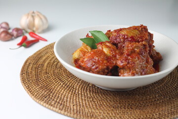 Ayam Bumbu Bali or Ayam bumbu Balado or Ayam Masak merah, Indonesian traditional chicken spicy, served on ceramic plate. Usually eat with yellow rice or nasi lemak. Isolated background. Copy space.