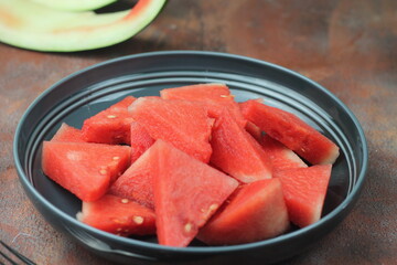 Buah Semangka or watermelon fruits, served on ceramic grey plate with fork beside, brown grainy background. Selective focus, close up. 