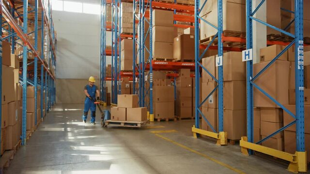 Worker Moves Cardboard Boxes using Manual Pallet Truck, Walking between Rows of Shelves with Goods in Retail Warehouse. People Work in Product Distribution Logistics Center. Side View Slow Motion