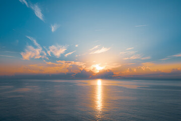 Sun rising from the sea. Colorful cloudy blue sky and sunbeams