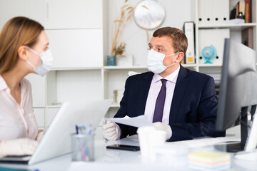 Focused businessman in disposable face mask and rubber gloves working with female assistant in office. Necessary precautions during COVID 19 pandemic..
