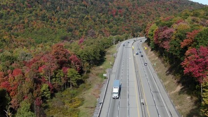 Cars, trucks, traffic drive on highway turnpike through colorful autumn leaves. Mountains and rolling hillsides in colorful fall foliage. Transportation, travel, logistics theme.