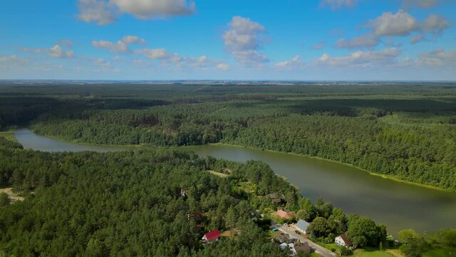 Flying over Kowalskie Blota village daytime, many private houses, and cottages located on the bank of Okierskie lake, Poland, panning around movement