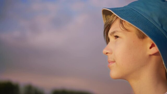 profile of a happy boy in a hat looking at the beautiful blue sky