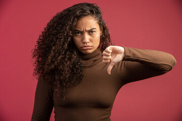 Portrait of a Brazilian woman with afro hairstyle and glamour makeup. Latin woman. Mixed race. Curly hair. Hair style. Red background. Thumbs down.