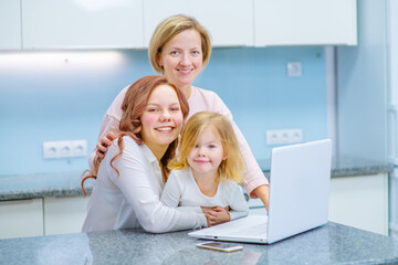 Women of different ages are sitting by a laptop in their kitchen. Generation difference concept