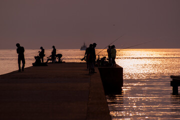 夕日に照らされた堤防で釣りを楽しむ人々