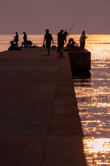 夕日に照らされた堤防で釣りを楽しむ人々