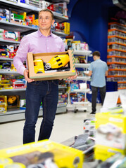 Portrait of glad cheerful adult man buying toy cement mixer machine in modern toy store