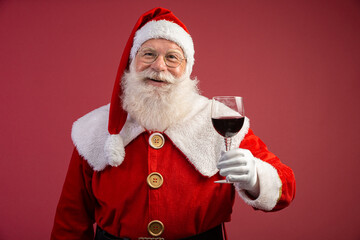 Claus holding a glass of wine in his hand. Santa Claus over a red background. Traditional year-end drink. Wine xmas promotion.