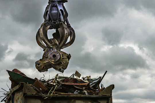 An excavator loads scrap metal into the back of a truck at a landfill or recycling center. - Powered by Adobe