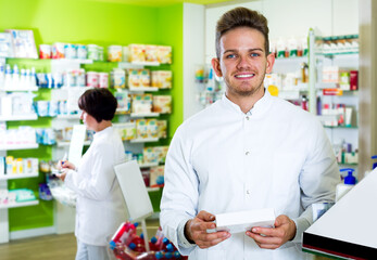 Cheerful man druggist in white coat giving advice to customers in pharmacy
