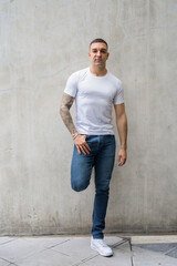 Full body shot of handsome man with tattoos leaning against wall