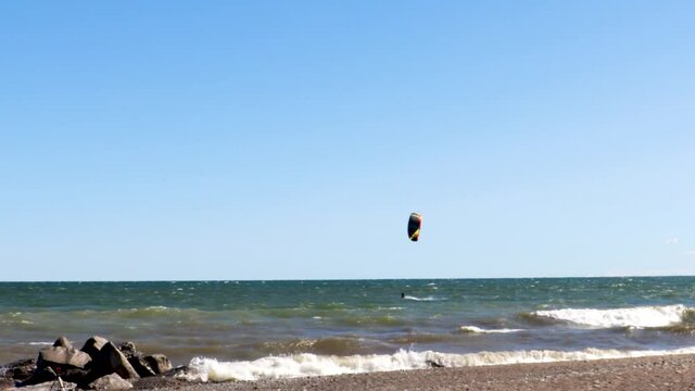 A lone kiteboarder skillfully traversing a rocky shoreline, on a beautify, virtually cloudless day.