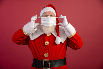 Real Santa Claus with a red background, wearing a protective mask, glasses and hat. Christmas with social distance. Covid-19