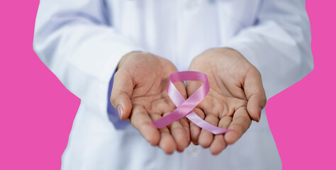 Pink ribbon in doctor's hand in patient room Healthcare Isolate on pink background, medicine and breast cancer concept