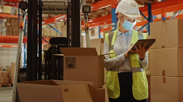 Female Warehouse Inventory Manager Wearing Face Mask for Safety, Using Digital Tablet Computer, Checking Cardboard Boxes. Delivery Distribution Center with Goods, Products Ready for Shipment