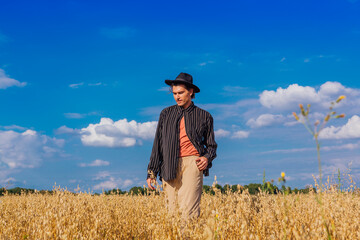 Tall handsome man with black hat standing at golden oat field.