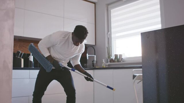 Happy handsom black man listening to the music and using broom as guitar. tidying up appartment. High quality 4k footage