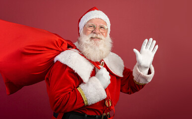 Real Santa Claus with a red background, wearing glasses, gloves and a hat looking side.