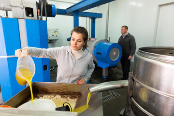 Confident workwoman controlling quality of olive oil of traditional cold pressing on artisanal...