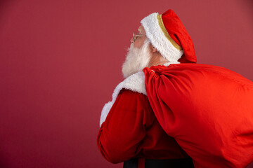 Santa Claus pulling huge bag of gifts on red background with copy space. Banner art.