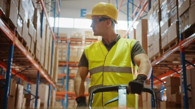 Worker Moves Cardboard Boxes using Hand Pallet Truck, Walking between Rows of Shelves with Goods in Retail Warehouse. People Work in Product Distribution Logistics Center. Point of View Shot