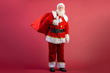 Santa Claus pulling huge bag of gifts on red background with copy space. Banner art.