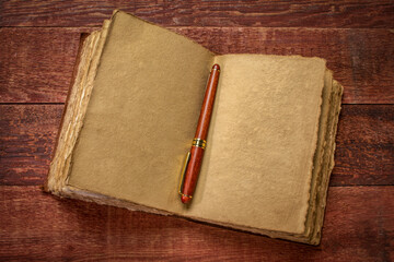 antique leatherbound journal with decked edge handmade paper pages and a stylish pen on a rustic wooden table, journaling concept