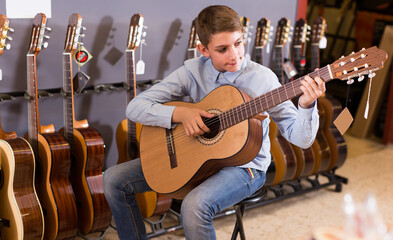 Male teenager examining various acoustic guitars in musical shop