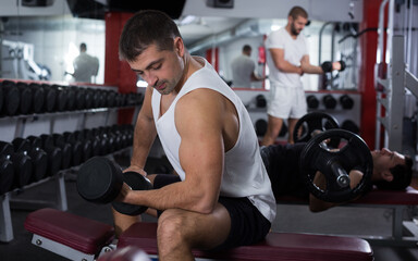 Fototapeta na wymiar Concentrated sporty guy during workout in gym with dumbbells