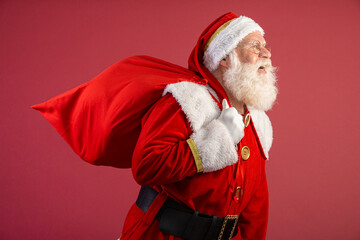 Santa Claus pulling huge bag of gifts on red background with copy space. Banner art.