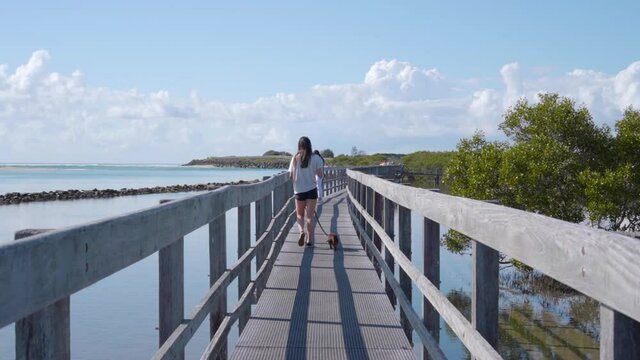 A young woman and a sausage dog walking down the Urunga Boardwalk