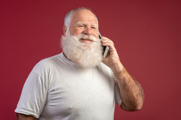 Fototapeta premium Smiling elderly bearded man using smartphone on red background. Senior man using wireless wi-fi internet connection on smart phone.