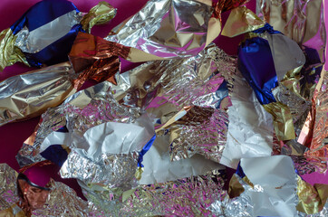Lots of crumpled shiny candy wrappers on pink background.