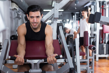 Fototapeta na wymiar Sporty guy training muscles of arms and shoulder girdle on fitness machine in gym