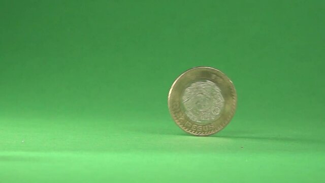 A Mexican 10 pesos coin rolling on a chroma background.
