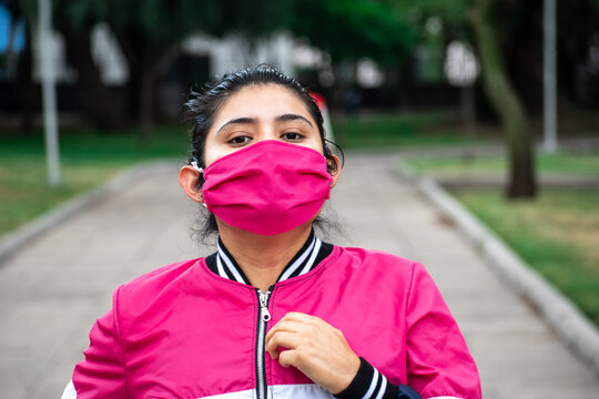 mujer joven con cubrebocas corriendo en el parque mirando hacia la c&aacute;mara