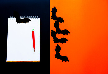Halloween flat composition of paper bats on an orange background and a Notepad with a pen. The view from the top