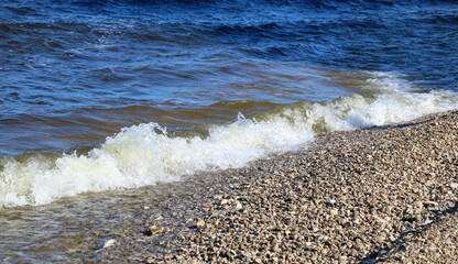 waves run onto the shore and crash against the rocks, creating many splashes and splashes near the shore. river surf in stormy weather near a stone pebble coast with foamy splashing waves.