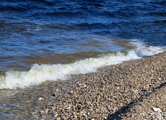 waves run onto the shore and crash against the rocks, creating many splashes and splashes near the shore. river surf in stormy weather near a stone pebble coast with foamy splashing waves.