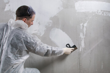 a worker in a protective uniform applies a finishing white putty to a concrete wall