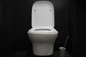 Contemporary white wall hung toilet. Black shiny tiles. Modern bathroom design. Cleanliness and hygiene.