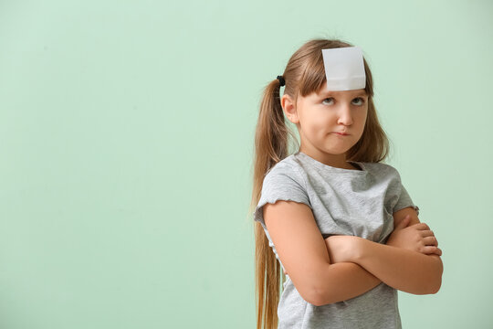 Displeased little girl with blank note paper on her forehead against color background